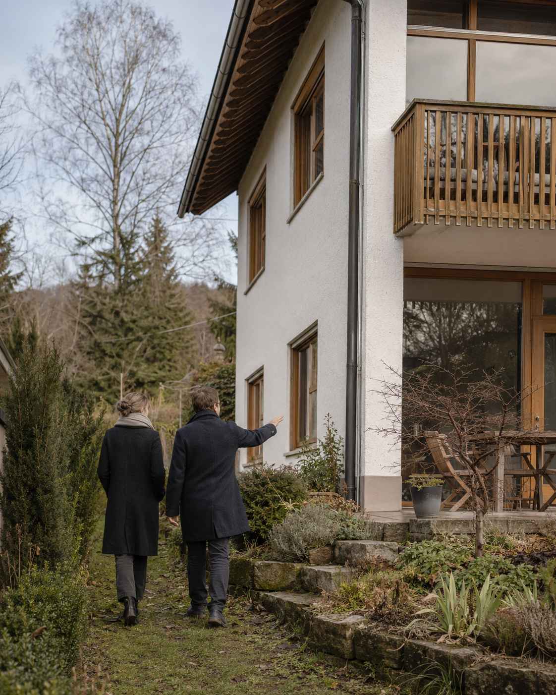 Grundstücke & Immobilien vor Ort betrachten: Zwei Personen besichtigen ein Wohnhaus mit Garten und Holzbalkon