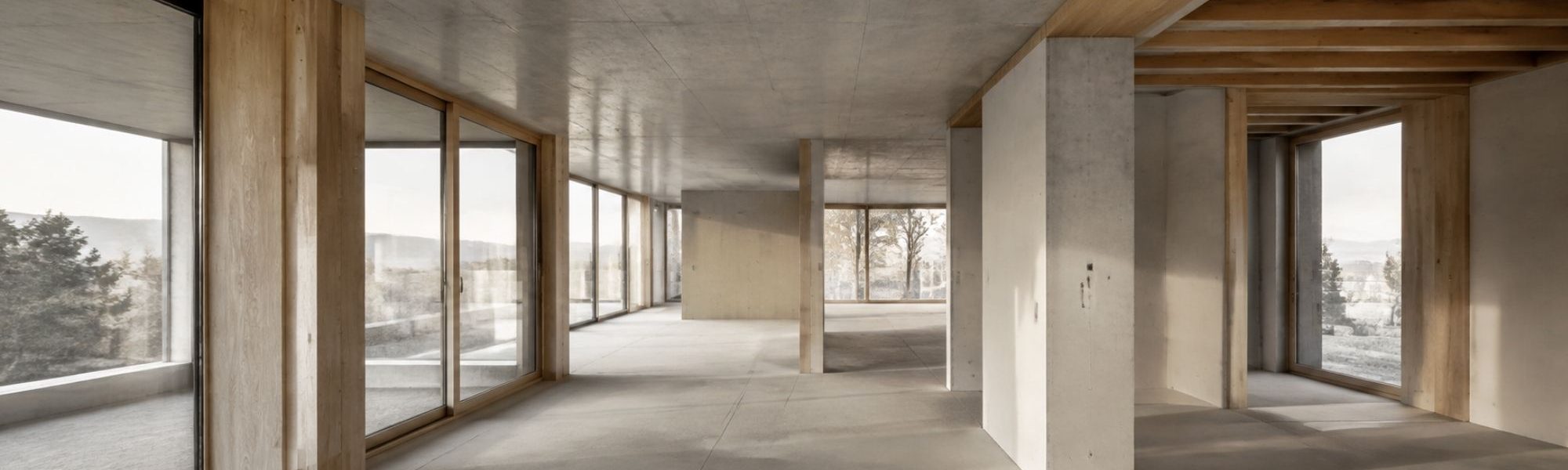 Innenraummotiv zum Hybridhaus mit sichtbaren Holzbauteilen, Betonoberflächen und großen Fensteröffnungen
