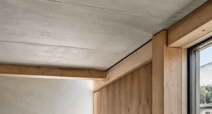 Deckenanschluss mit sichtbarer Betonoberfläche, Holzbalken und Holzstütze neben einem Fenster