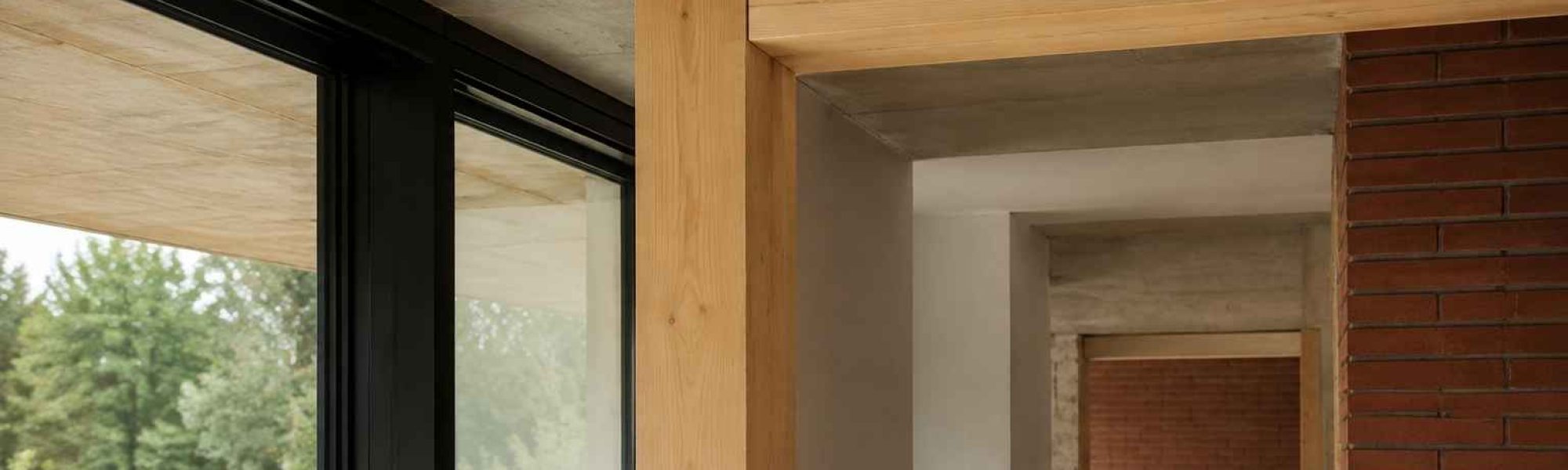 Innenraumdetail mit Holzbauteilen, Ziegelmauerwerk, Betonoberflächen und dunklen Fensterrahmen
